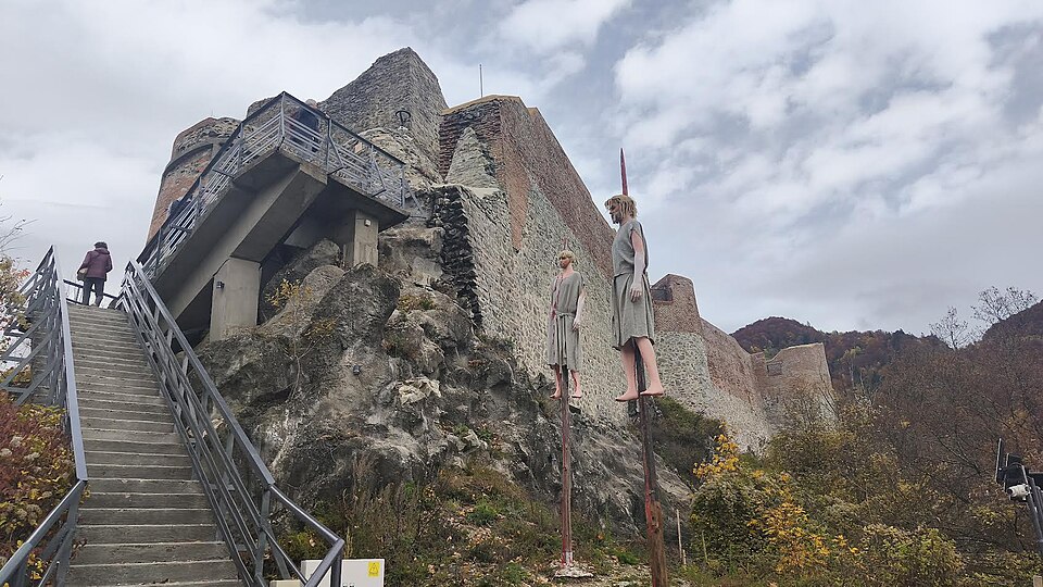 Zbytky hradeb hradu Poenari nad betonovým schodištěm, v popředí figuríny naražené na kůl připomínající Vlada Napichovače
