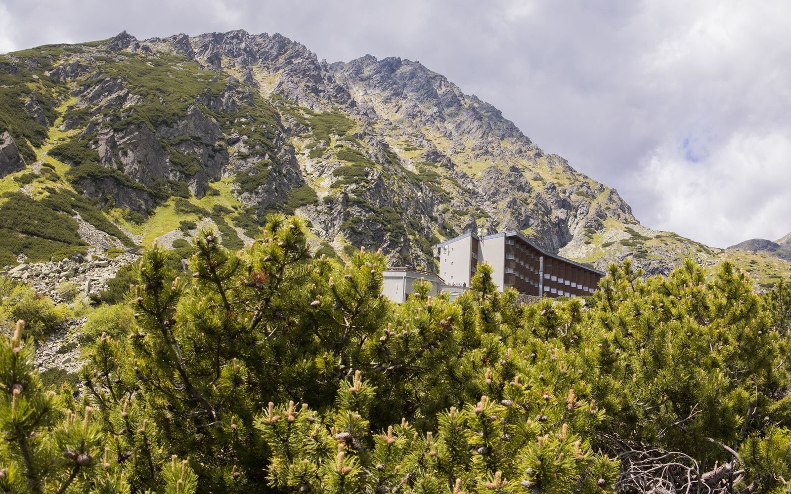 Horský hotel pod skalnatým svahem obrostlým kosodřevinou