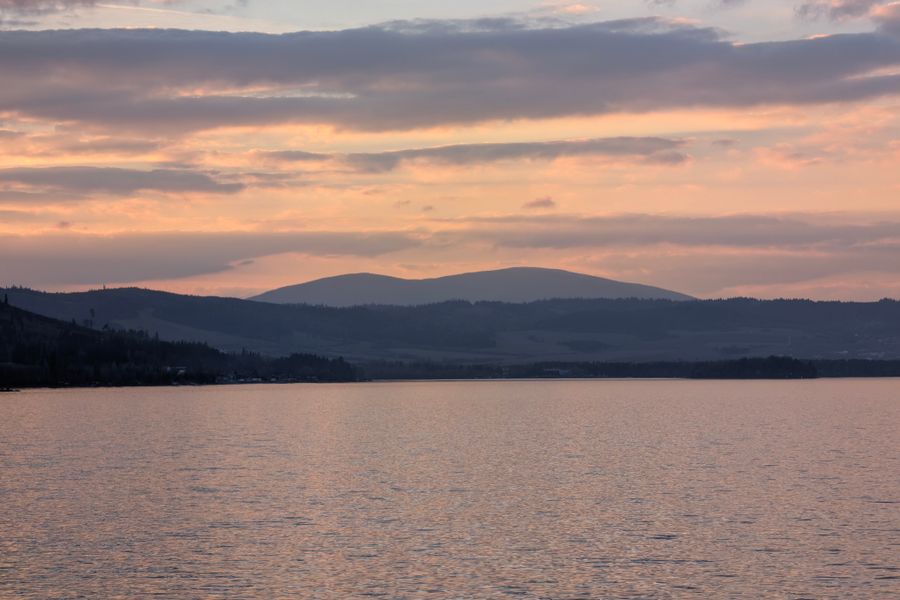 Západ slunce nad klidnou hladinou jezera s kopci v dálce
