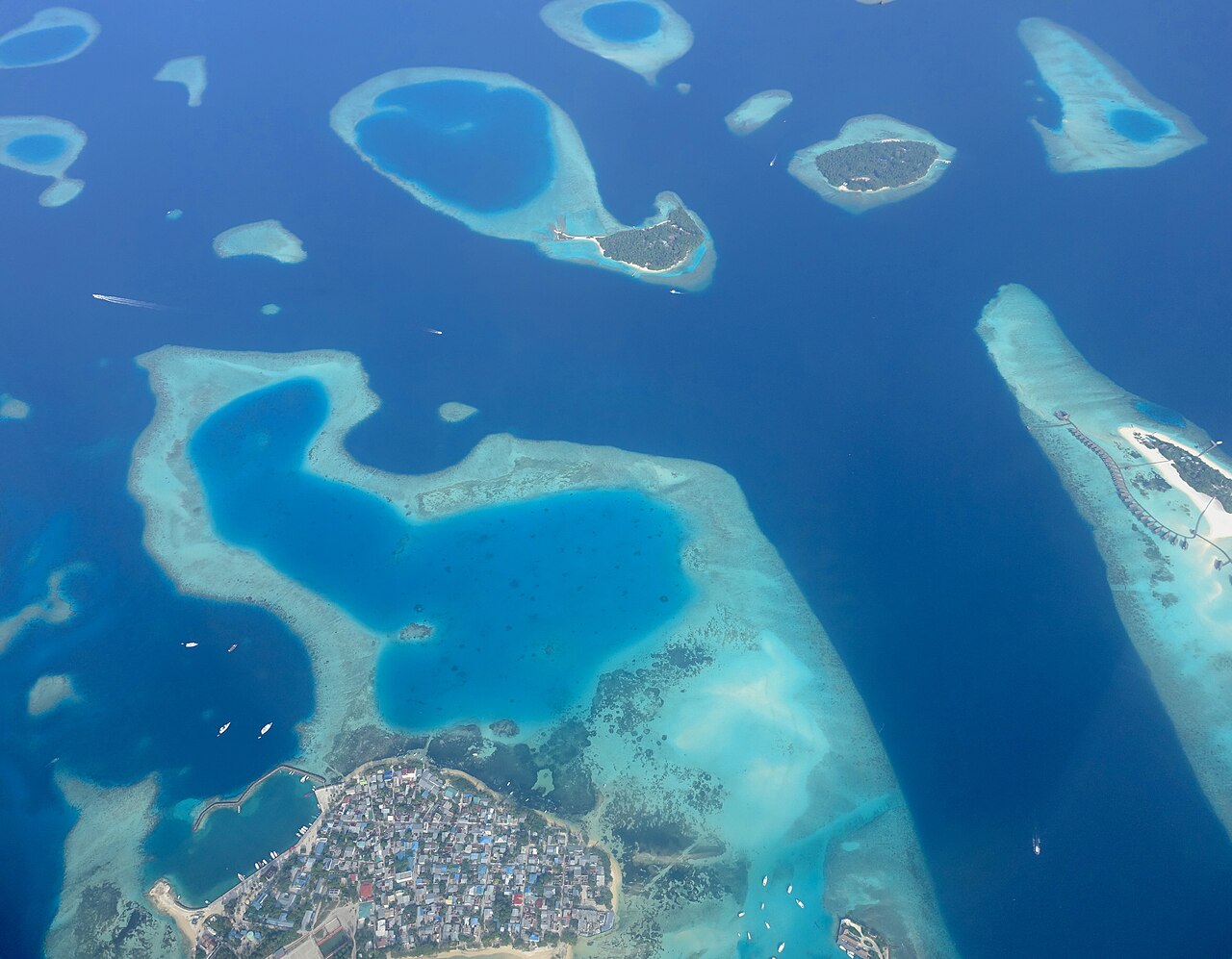 Letecký pohled na obydlený maledivský ostrov Guraidhoo s hustou zástavbou a vedle něj resortní ostrov s vilami nad vodou