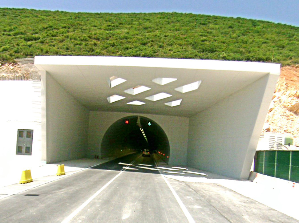 Southern portal of the Llogara tunnel with a concrete canopy over the entrance and a car disappearing inside