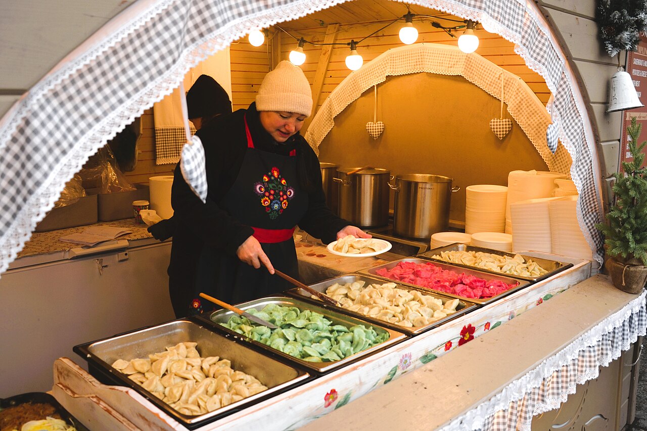 A stallholder in a folk apron scooping pierogi from metal trays at the Krakow Christmas market