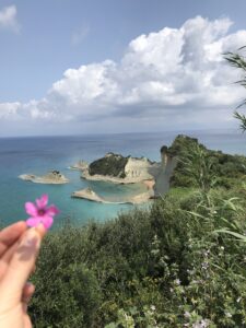 Formaciones rocosas blancas del cabo Drastis, en el norte de Corfú, con una mano que sostiene una flor rosa en primer plano