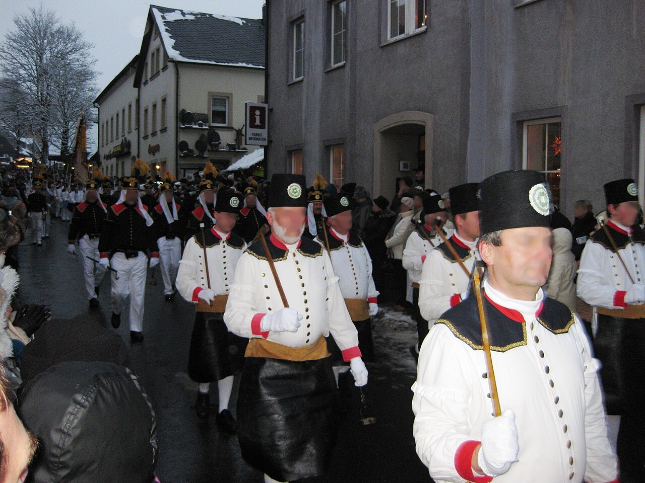 Horníci v bílých a černých krojích s hornickými kladívky pochodují při Bergparade po hlavní ulici v Seiffenu