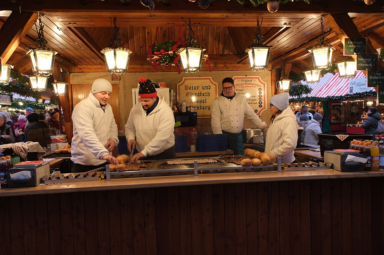 Vendors dressed in white grilling Nuremberg sausages and filling bread rolls at a stall at the Christkindlesmarkt