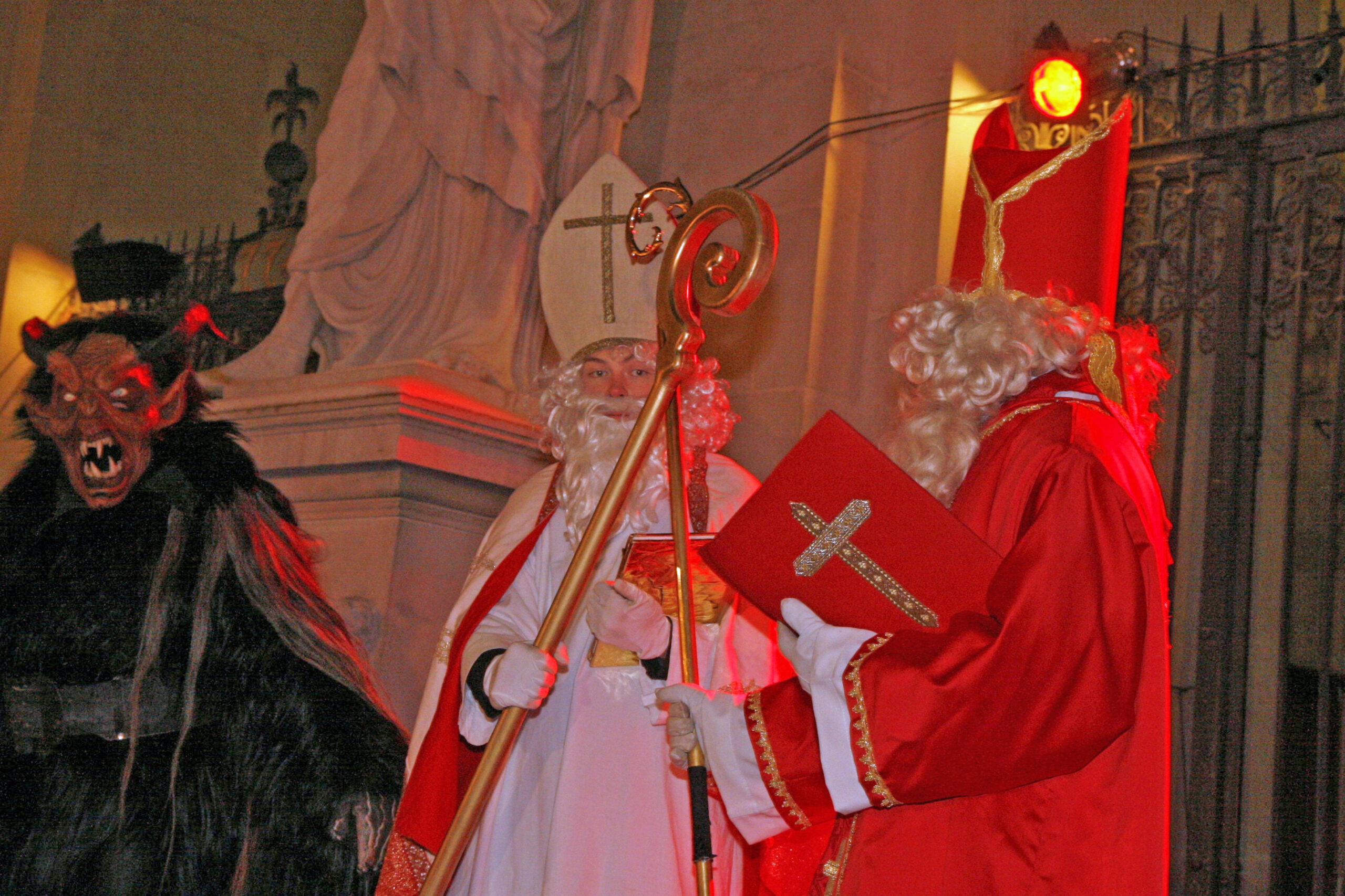 Mikuláš v biskupském oděvu a Krampus s rohatou dřevěnou maskou na Salzburger Christkindlmarktu