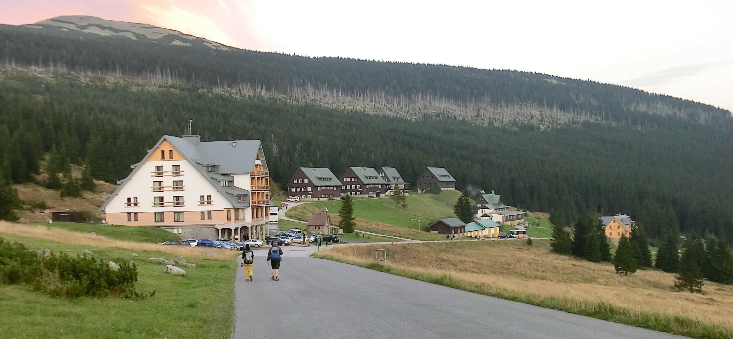Erlebachova bouda a další horské boudy na louce nad Špindlerovým Mlýnem, v pozadí zalesněný hřeben Krkonoš
