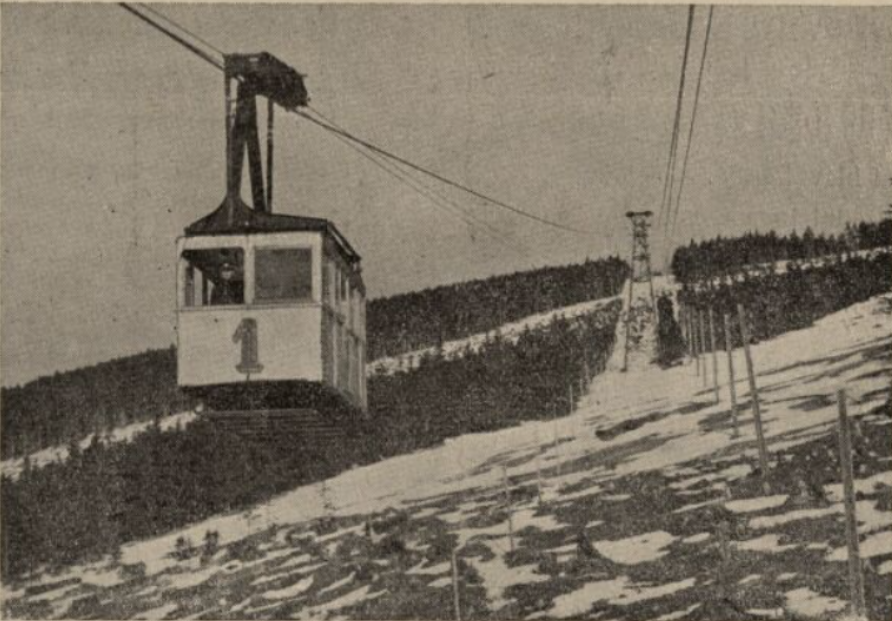 Historická černobílá fotografie kabiny číslo 1 původní lanovky z Janských Lázní na Černou horu nad zasněženým svahem s ocelovou podpěrou