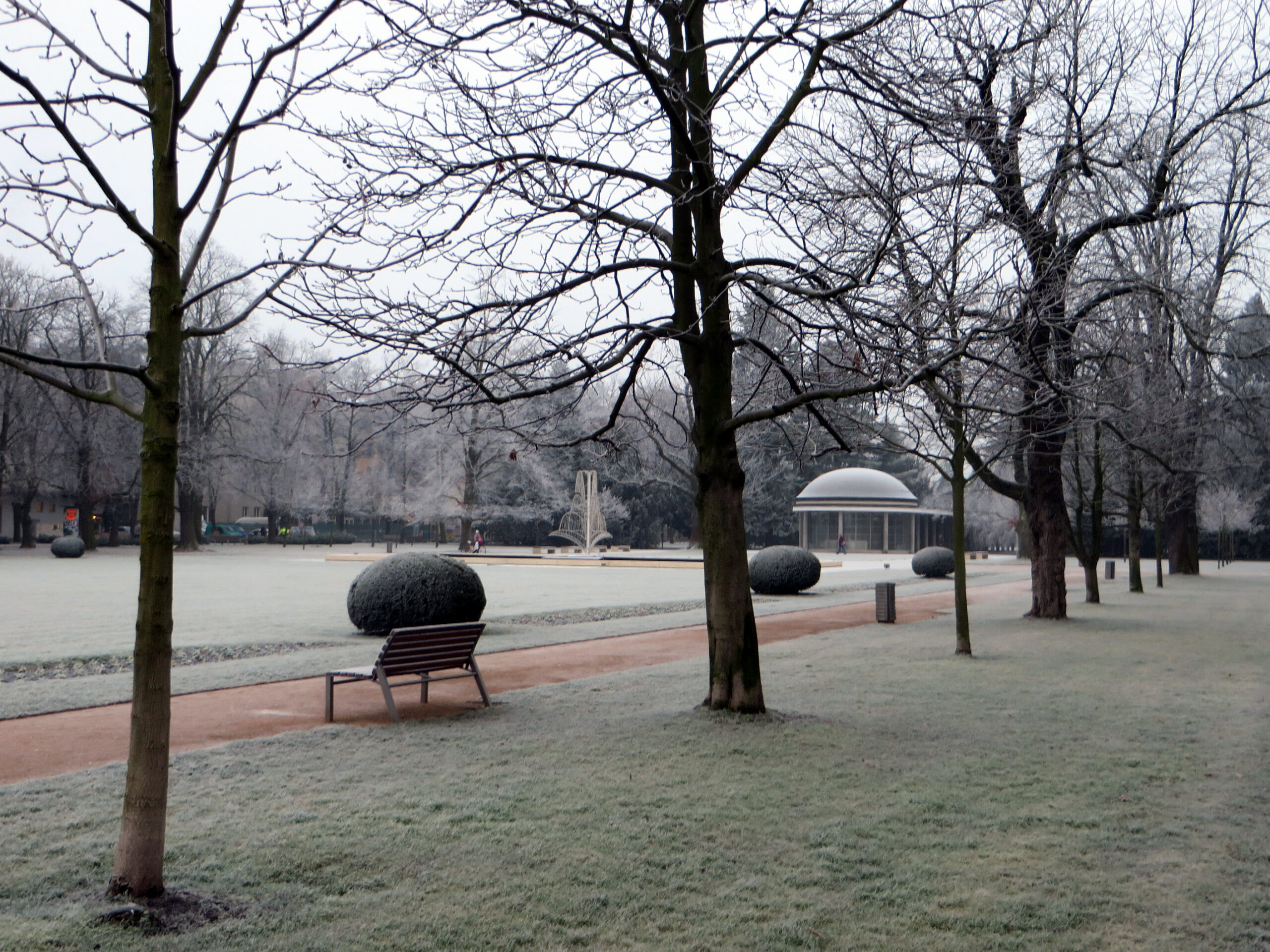 Ojíněný lázeňský park v Poděbradech v zimě s lavičkou, kašnou a kruhovým pavilonem Libenského kolonády