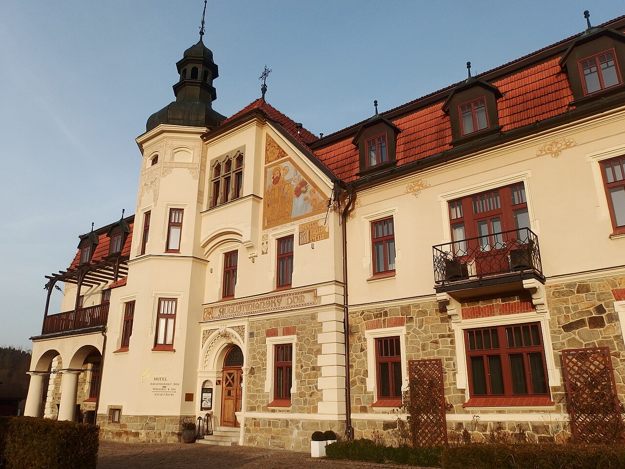 Secesní budova Augustiniánského domu v Luhačovicích s věžičkou, freskou na štítu a kamennou podezdívkou