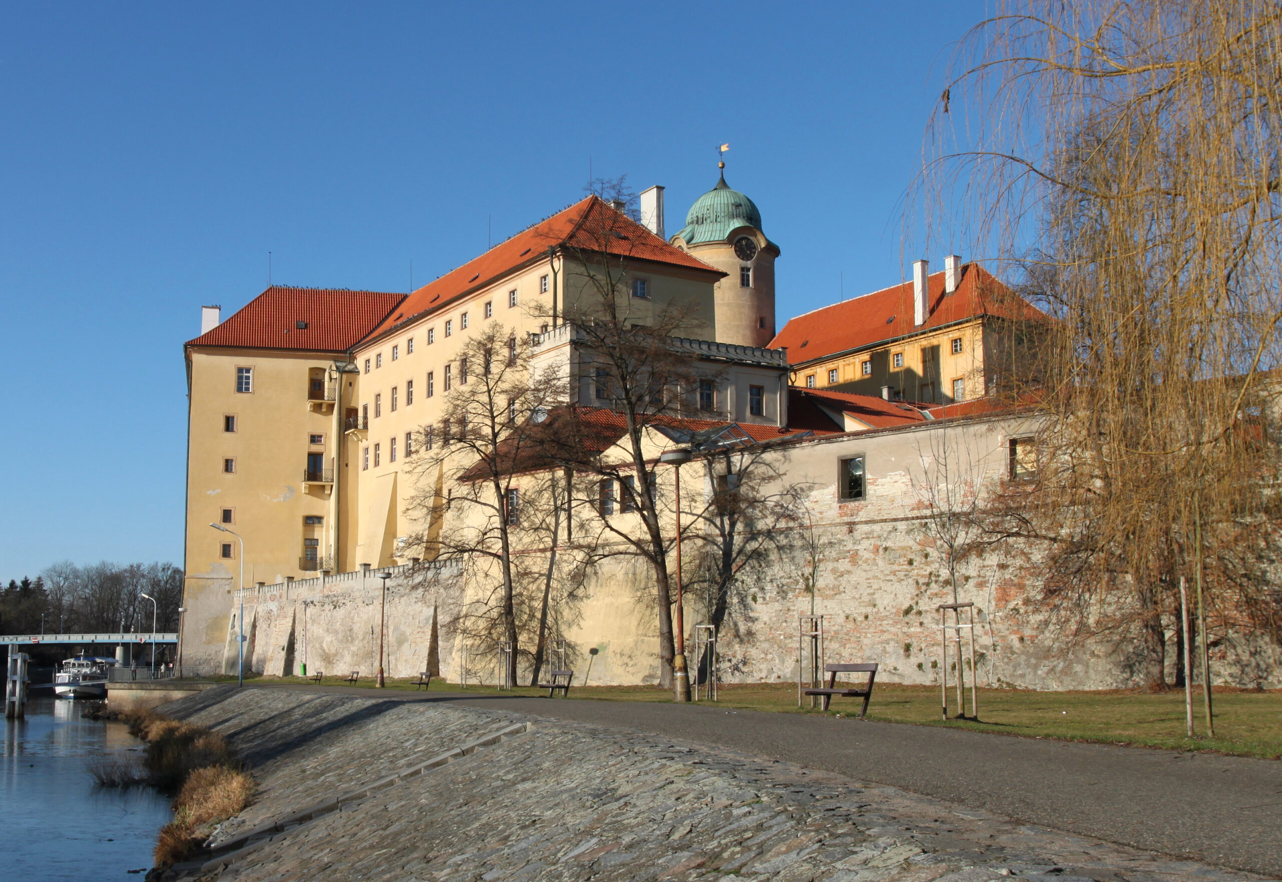 Poděbradský zámek nad Labem v prosinci s holými stromy a promenádou na nábřeží
