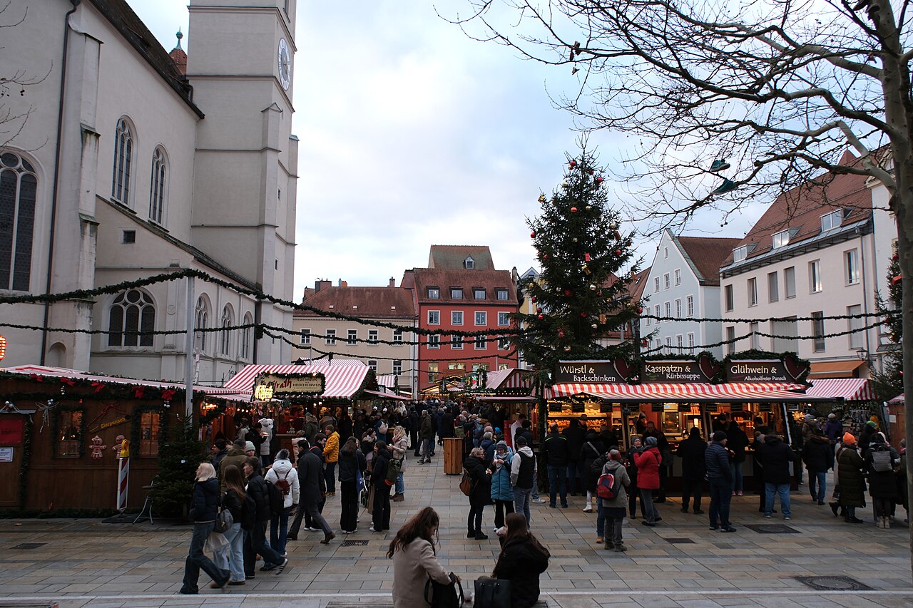 Christkindlmarkt na Neupfarrplatzu v Řezně: vánoční strom, stánky s klobásami, Kasspatzn a svařákem a vlevo kostel Neupfarrkirche