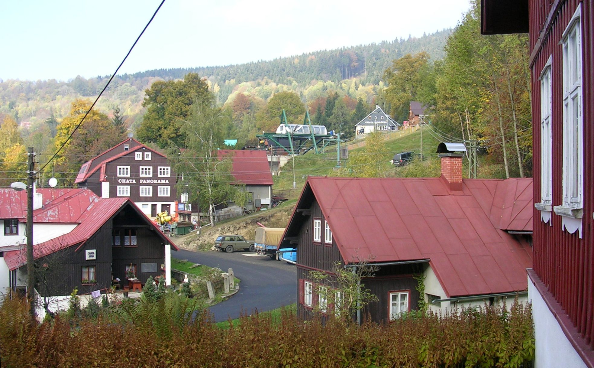 Rejdice na podzim: dřevěné chalupy, Chata Panorama a zelená dolní stanice dvousedačkové lanovky ve svahu