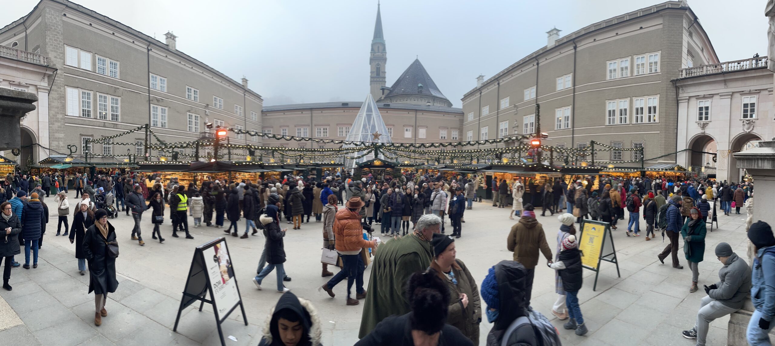 Salzburg vánoční trhy: Christkindlmarkt na Residenzplatzu, řady dřevěných stánků s girlandami a davy lidí mezi barokními budovami