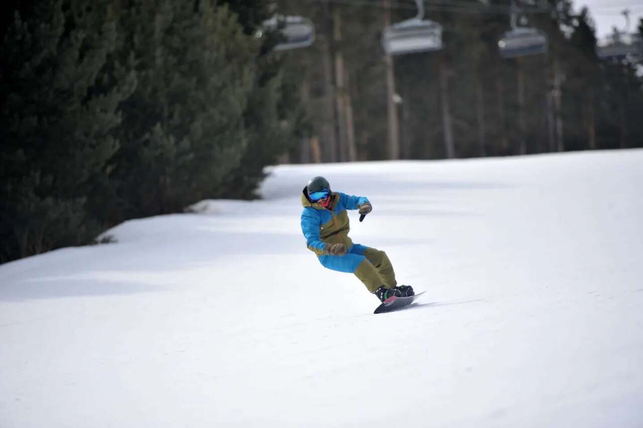 Snowboardista na upravené sjezdovce v Sarıkamışi, vedle borový les a sedačková lanovka