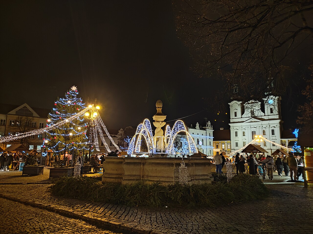Barokní kašna na Masarykově náměstí v Uherském Hradišti ozdobená světelným adventním věncem, vánoční strom a stánky jarmarku
