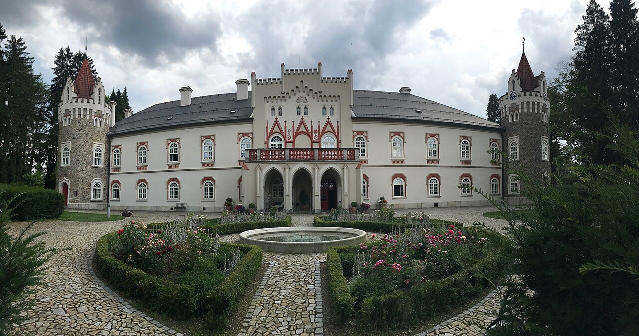 Zámek Herálec s dvěma věžemi, kašnou a růžovými záhony na nádvoří